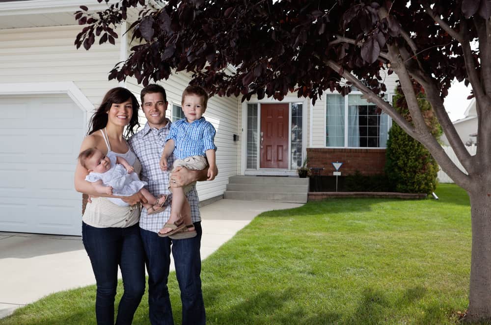 Portrait of happy couple standing with their children in front of house